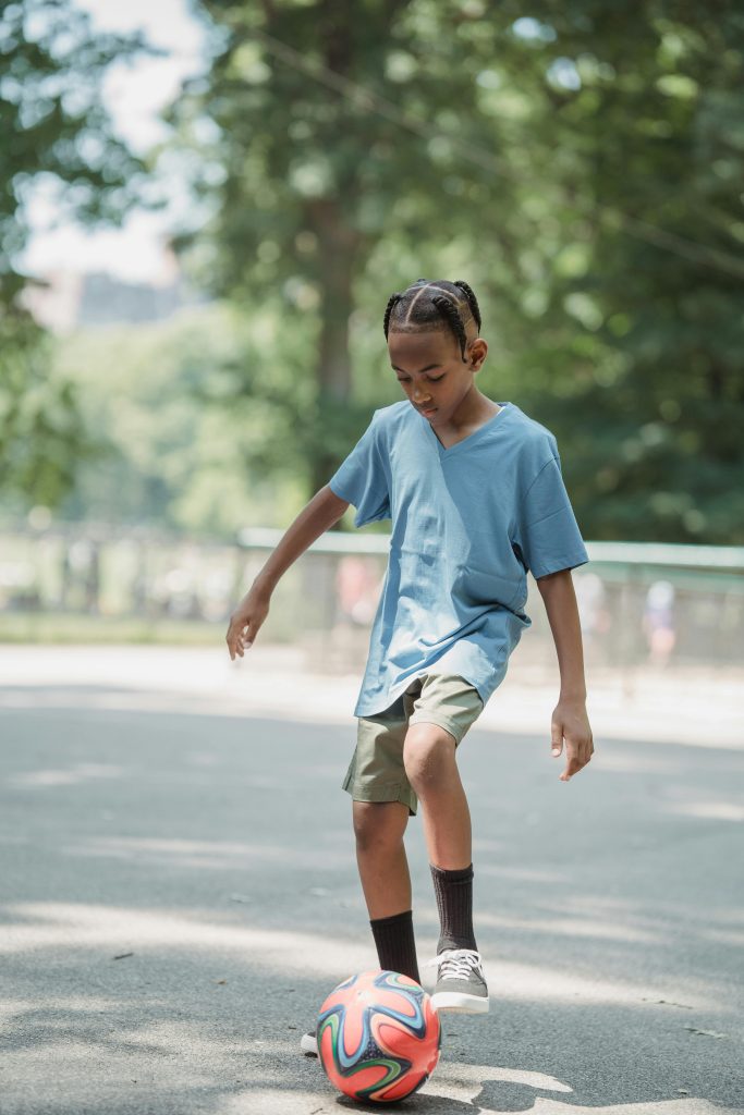 Young boy skillfully playing football in a sunny park, showcasing sportsmanship and fun.